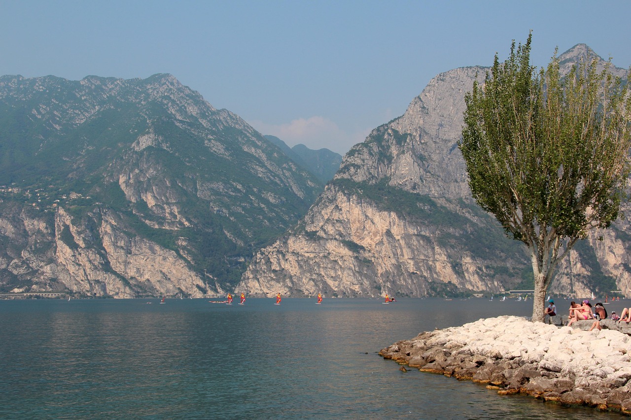 Persone che praticano sport acquatici sul Lago di Garda, circondati da splendide montagne e sole estivo.