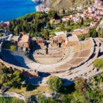 Interno di un teatro italiano con decorazioni eleganti e pubblico in attesa dello spettacolo.