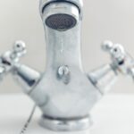 Rubinetto che perde acqua con attrezzi per riparazione su un tavolo di lavoro.